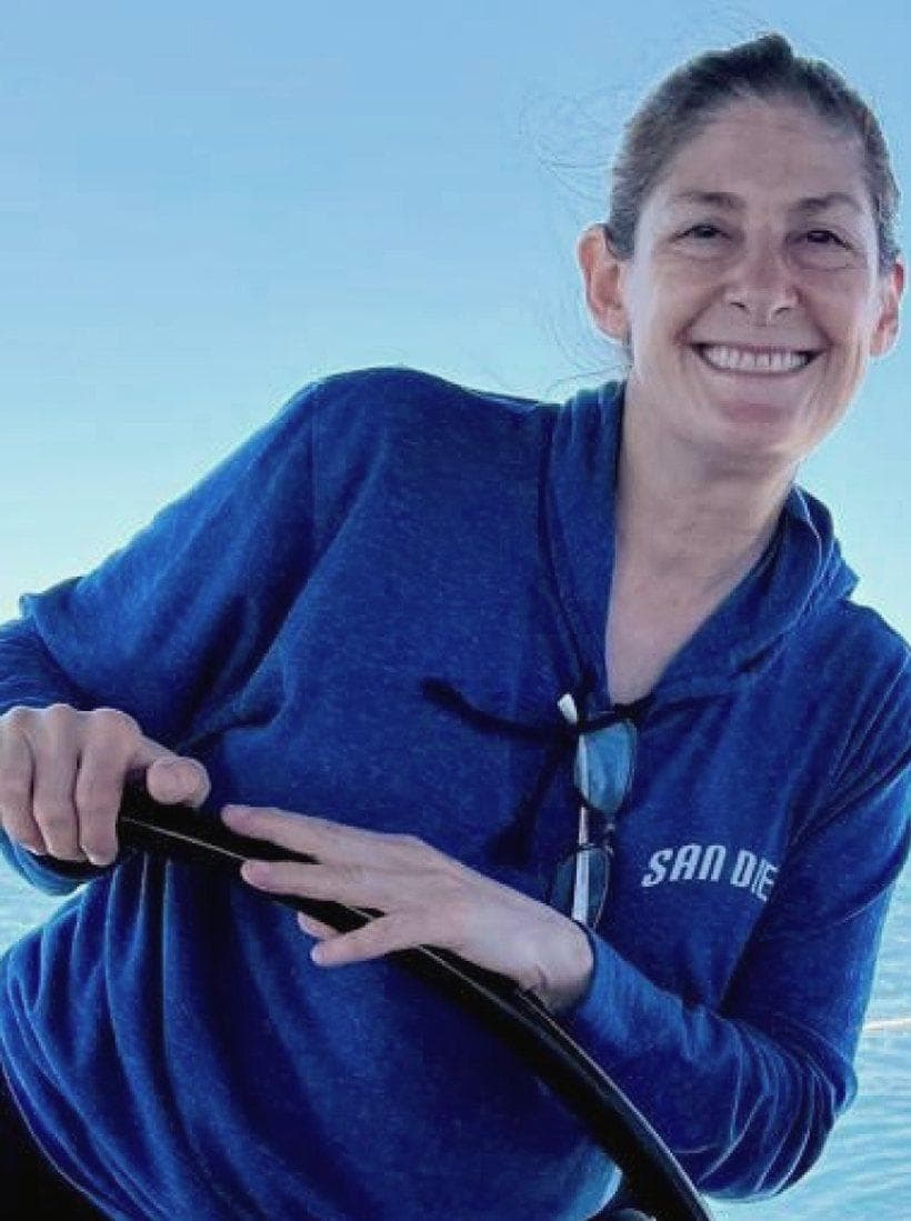 Christina Lawrence at the wheel of a boat, San Diego bay behind her.